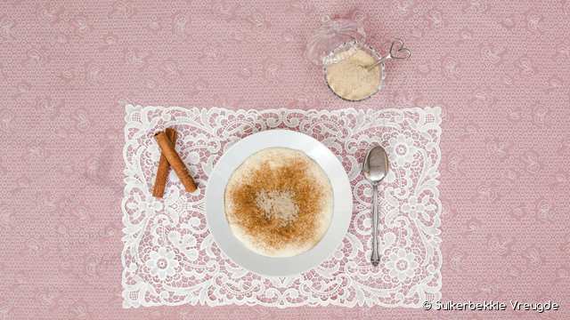 Melkkos met kaneelsuiker op 'n kantdoek, met kaneelstokkies en 'n suikerbakkie
